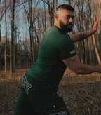 Man wearing green shirt and cargo sweats with "BEEFY" on it in the forest