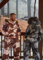 Two people wearing cow print outfits on a wooden deck with a forest background.